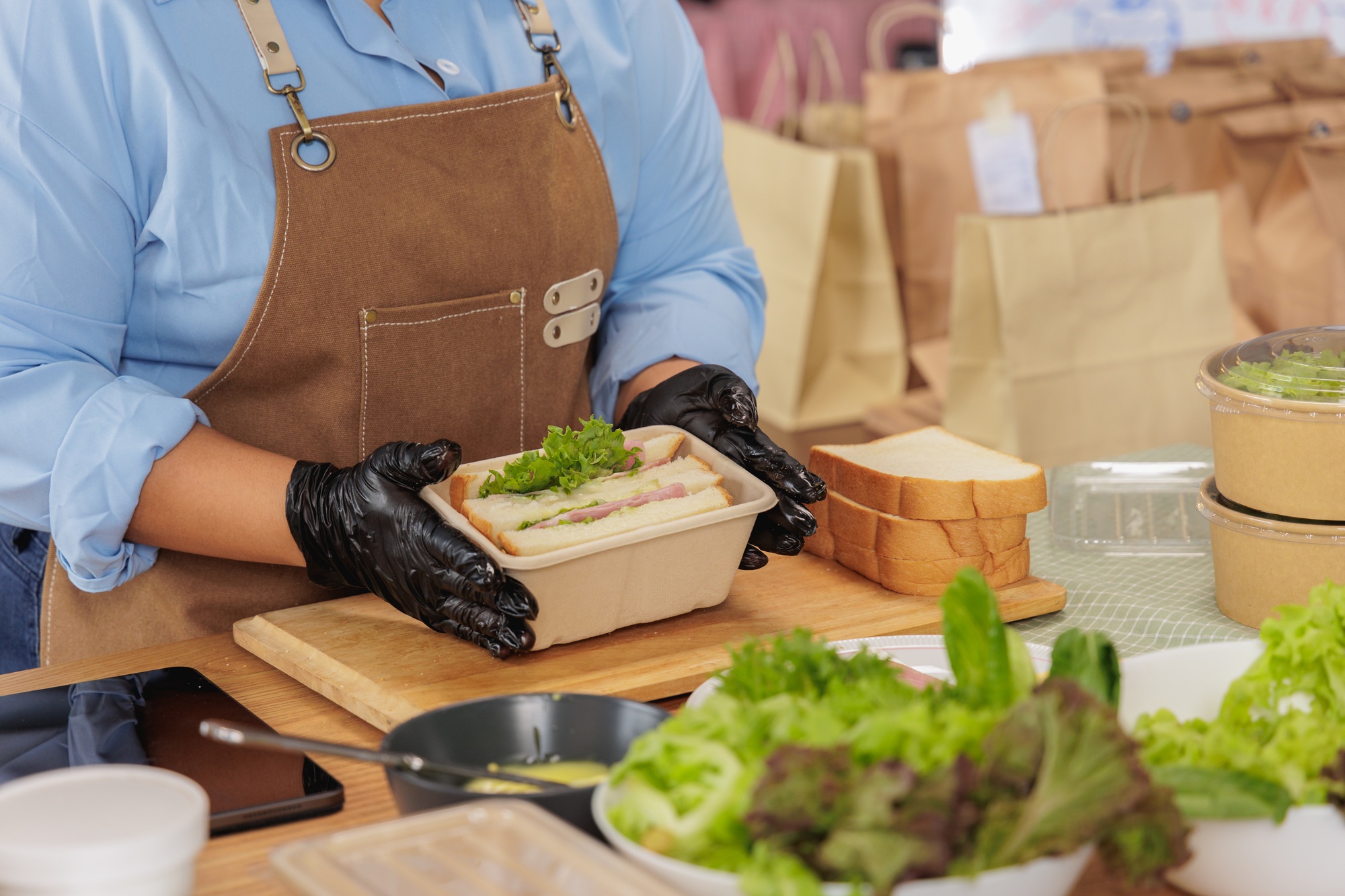 Chef preparing fresh meal with greens and bread in a kitchen. Healthy takeout food packaging.